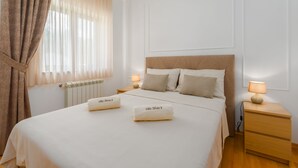 Ein ordentlich bezogenes Bett mit zwei Handtüchern, einem Nachttisch mit Lampe und einem Fenster mit Vorhängen.