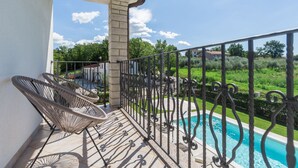 Ein Balkon mit Blick auf einen Pool, einem Metallgeländer und Korbstühlen.