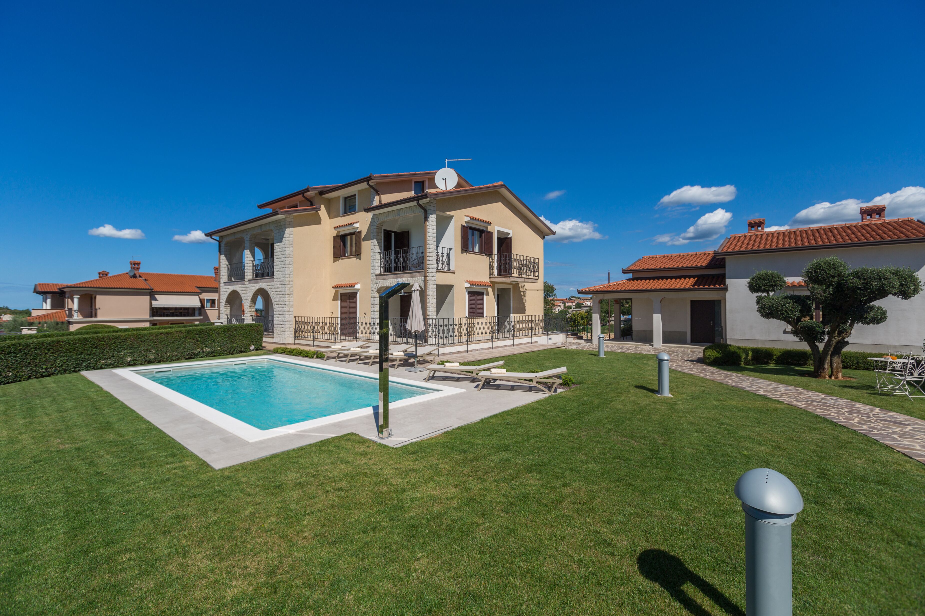 A two-story house with a swimming pool, a well-maintained lawn, and a clear blue sky.