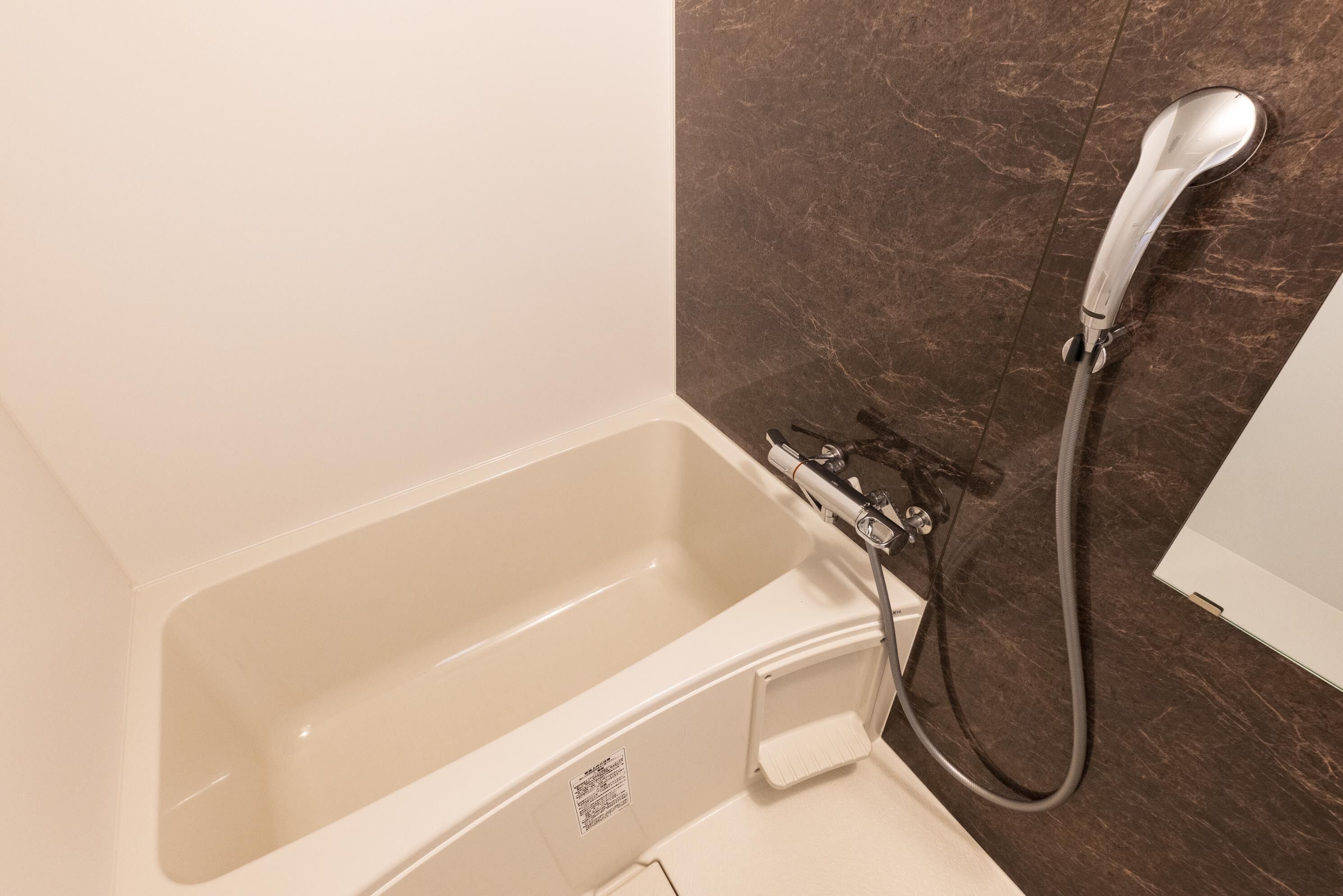 A bathroom with a bathtub, a shower, and a marble wall.