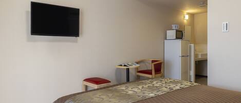 A hotel room with a bed, a television, a small table with a chair, and a microwave on a cabinet.