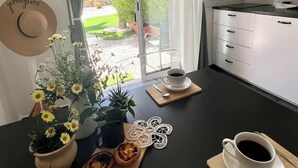 Une cuisine moderne avec une grande fenêtre, une table à manger avec des tasses à café, une plante en pot et un élément décoratif mural.
