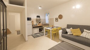 A compact living space with a kitchenette, a dining area with yellow chairs, and a grey sofa with patterned cushions. - BON Repos Apartment With Swimming Pool (Alghero)