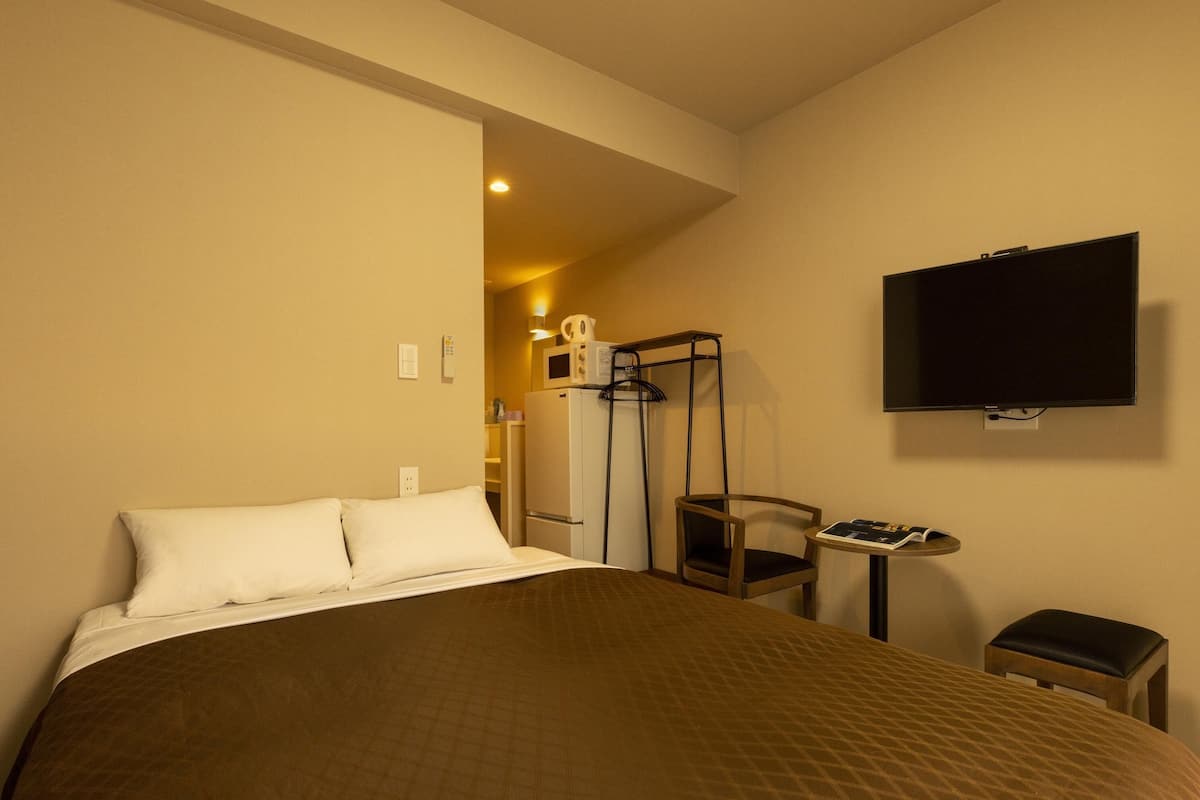 A hotel room with a large bed, a TV mounted on the wall, a small table, and a chair.