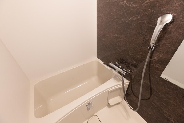 A bathroom with a bathtub, a shower, and a marble wall. - Mr.KINJO inn MIYAKOJIMA (Miyakojima)