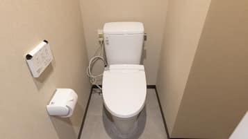 Une petite salle de bain propre, avec des toilettes blanches, un distributeur d’essuie-tout et un sèche-mains.