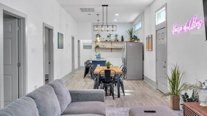 A modern kitchen with a dining area, a gray sofa, and a neon sign reading "House of Vibes".