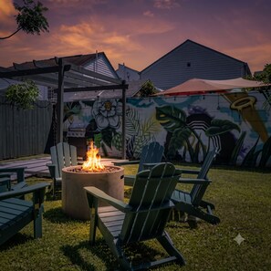 A backyard with a fire pit, outdoor furniture, and a mural on the wall.
