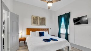 A hotel room with a bed, a nightstand, a ceiling fan, a TV, and a window with curtains.