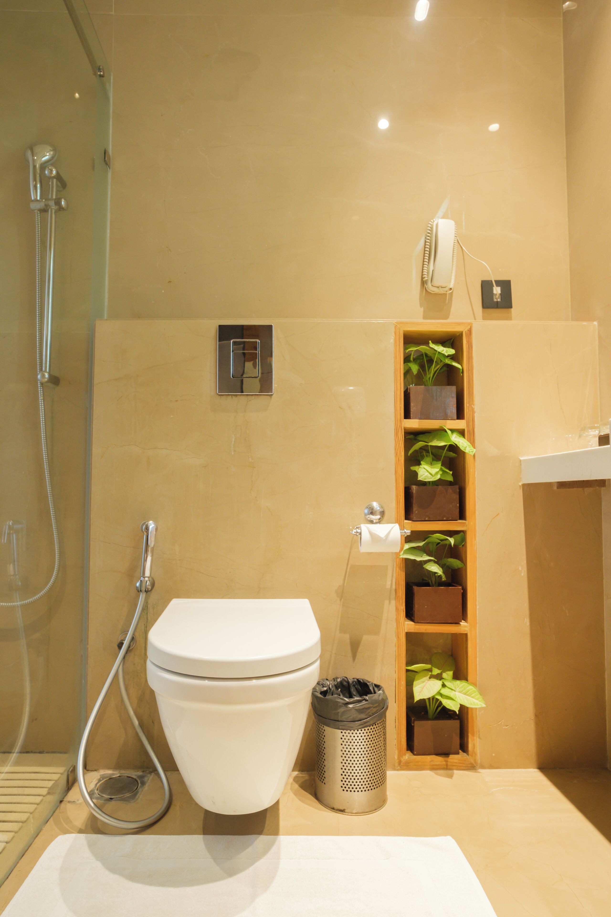 Un baño con inodoro, ducha, lavamanos y estante con plantas.