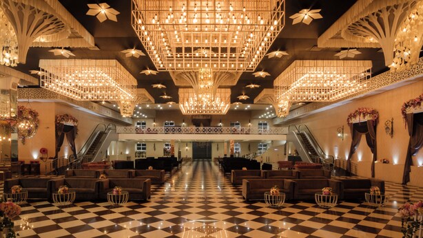 Un vaste hall d’entrée avec un sol à carreaux, de nombreux espaces aménagés pour s’asseoir et un grand lustre.