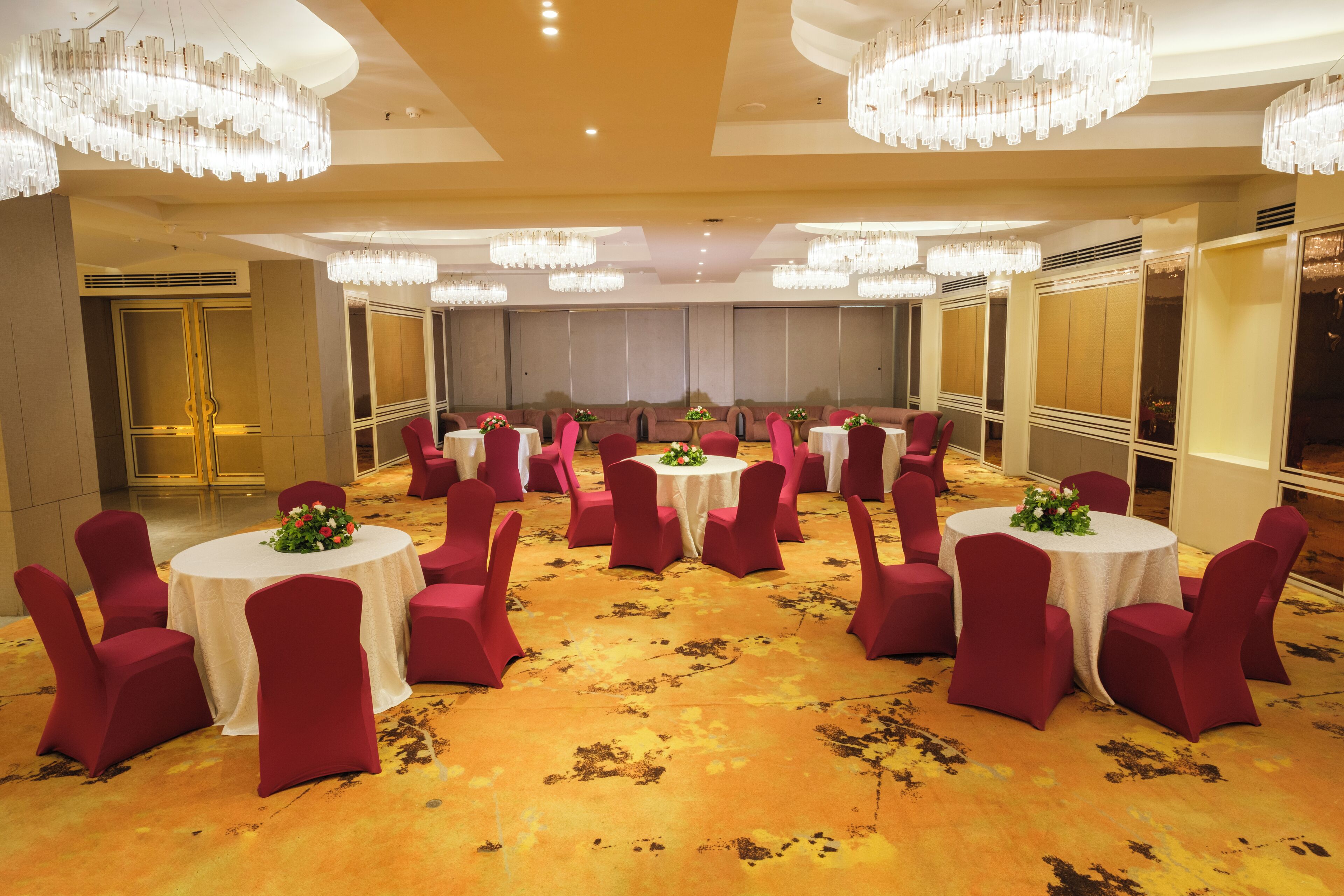 Un salón de banquetes con mesas redondas, sillas rojas y candelabros.