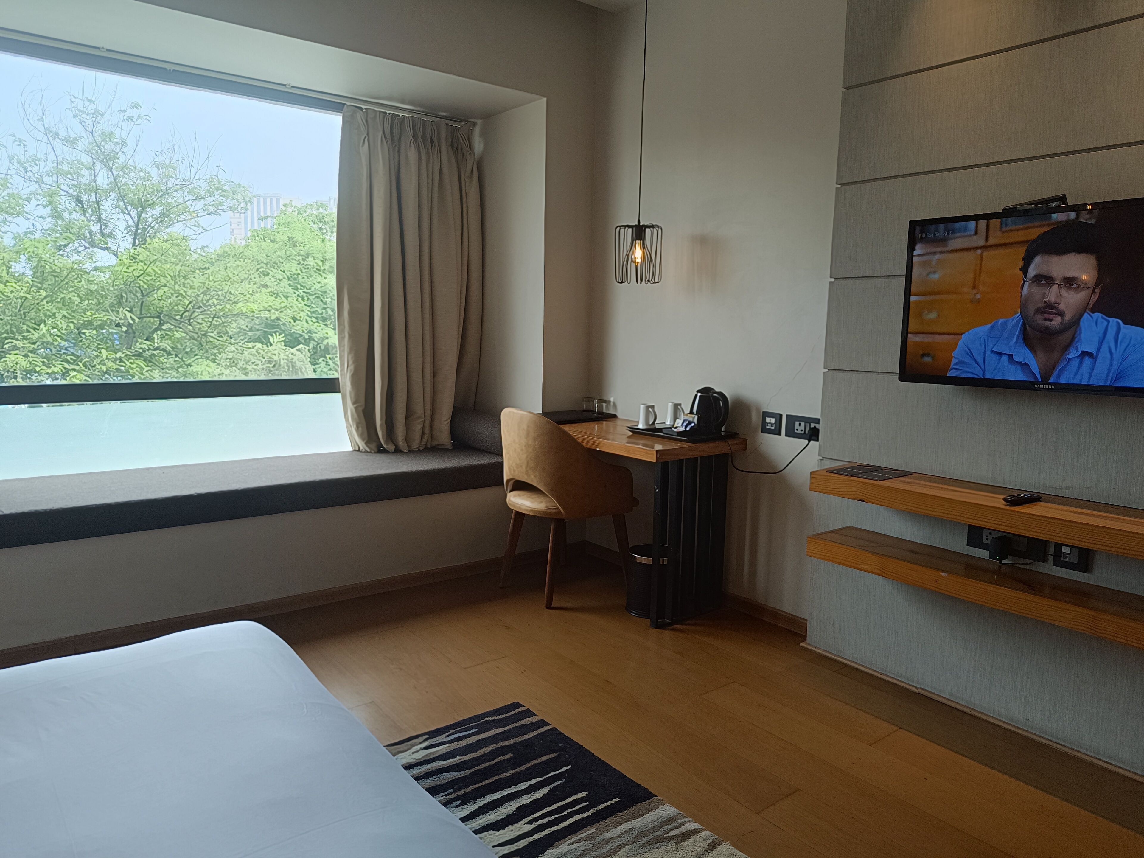A hotel room with a bed, a desk with a chair, a TV, and a window with curtains.