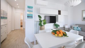 A modern, well-lit living space with a dining area featuring a white table and chairs, a flat-screen TV mounted on the wall, and a sofa with a patterned cushion. - Italianway - Cristoforo Colombo 12 INT 1A (San Bartolomeo al Mare)