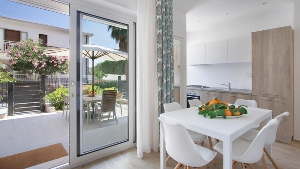 A modern kitchen with white cabinets and a dining area with a white table and chairs. - Italianway - Cristoforo Colombo 12 INT 1A (San Bartolomeo al Mare)