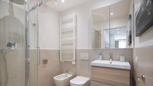 A modern bathroom with a glass shower enclosure, a bidet, a toilet, a vanity with a mirror, and a towel rack. - Italianway - Cristoforo Colombo 12 INT 1A (San Bartolomeo al Mare)