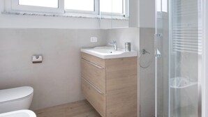 A modern bathroom with a toilet, a wooden vanity with a sink, and a glass shower enclosure. - Italianway - Cristoforo Colombo 12 INT 5 (San Bartolomeo al Mare)