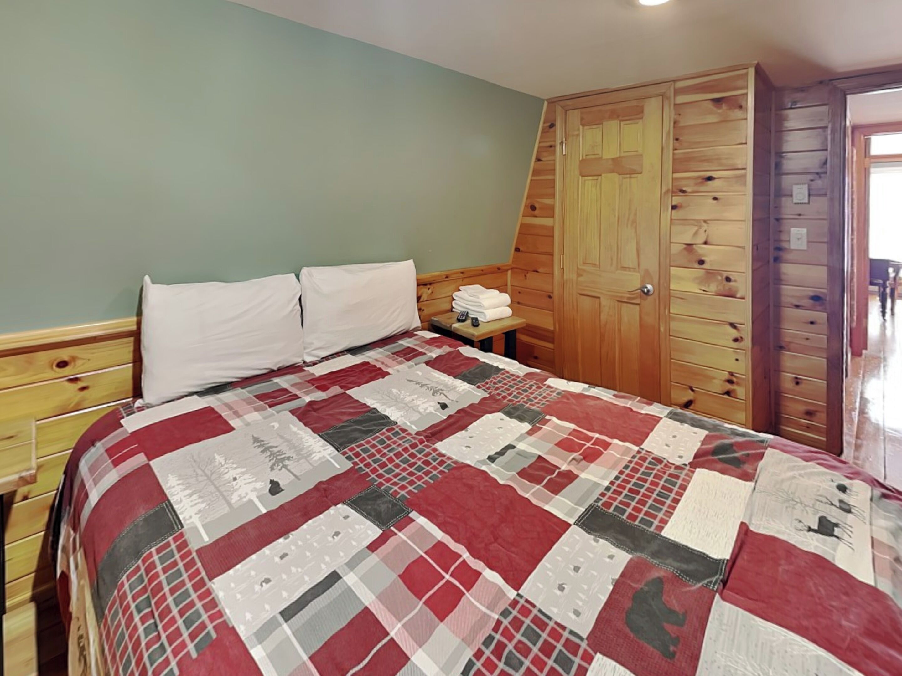A bedroom with a wooden bed frame, a quilt, a wooden wardrobe, and a small bedside table with towels.