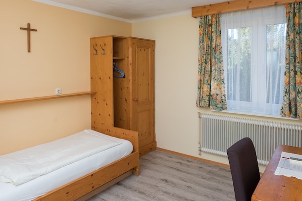 Una habitación con una cama individual, un armario de madera, un radiador y una ventana con cortinas florales.