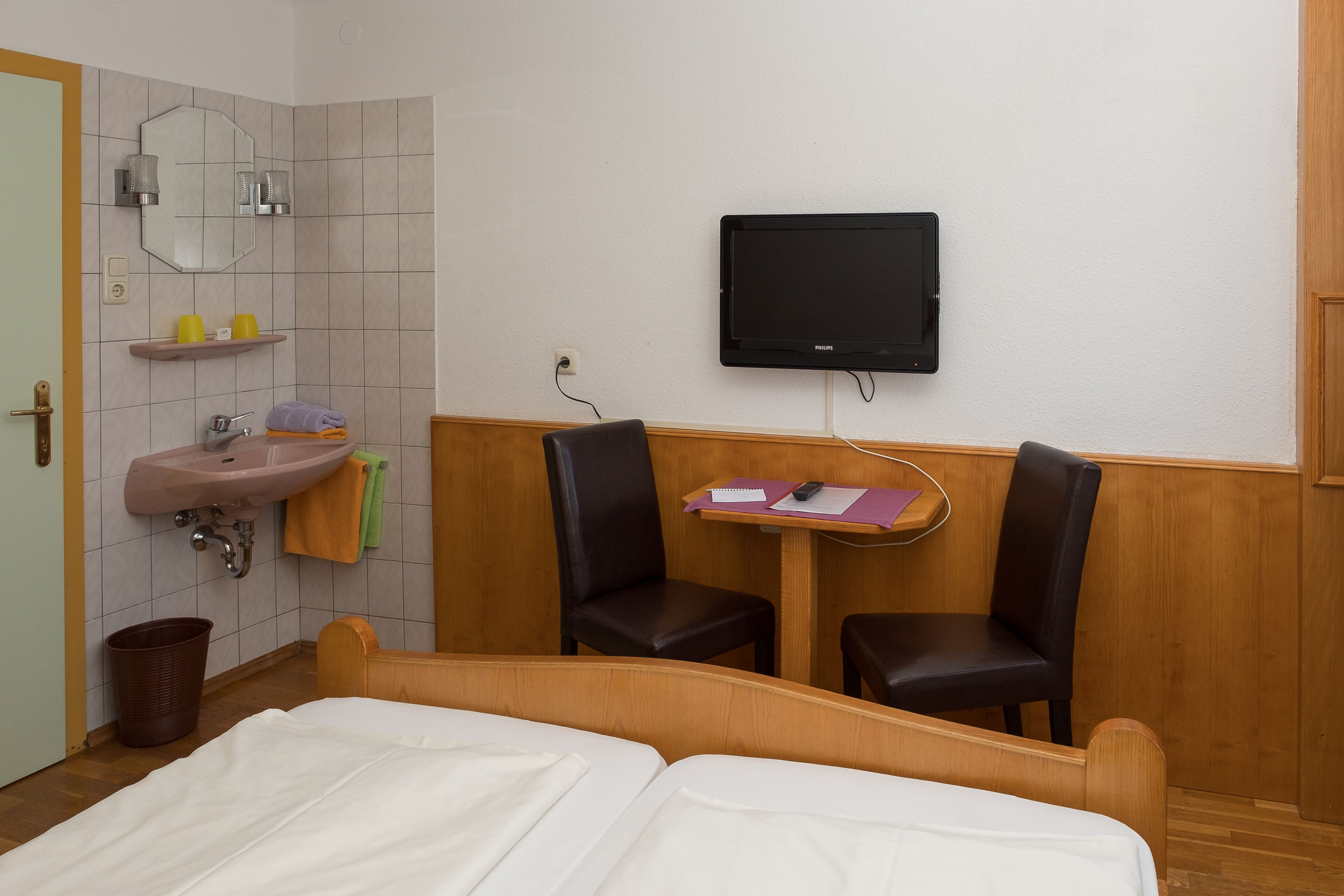 Une chambre d’hôtel comprenant un lit, un lavabo, un miroir, une télévision et deux chaises.