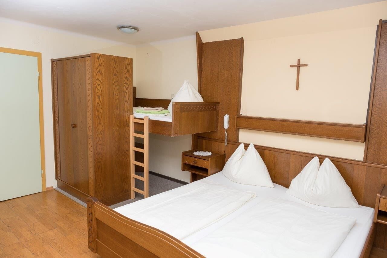 Una habitación con literas, un armario de madera y una cruz en la pared.