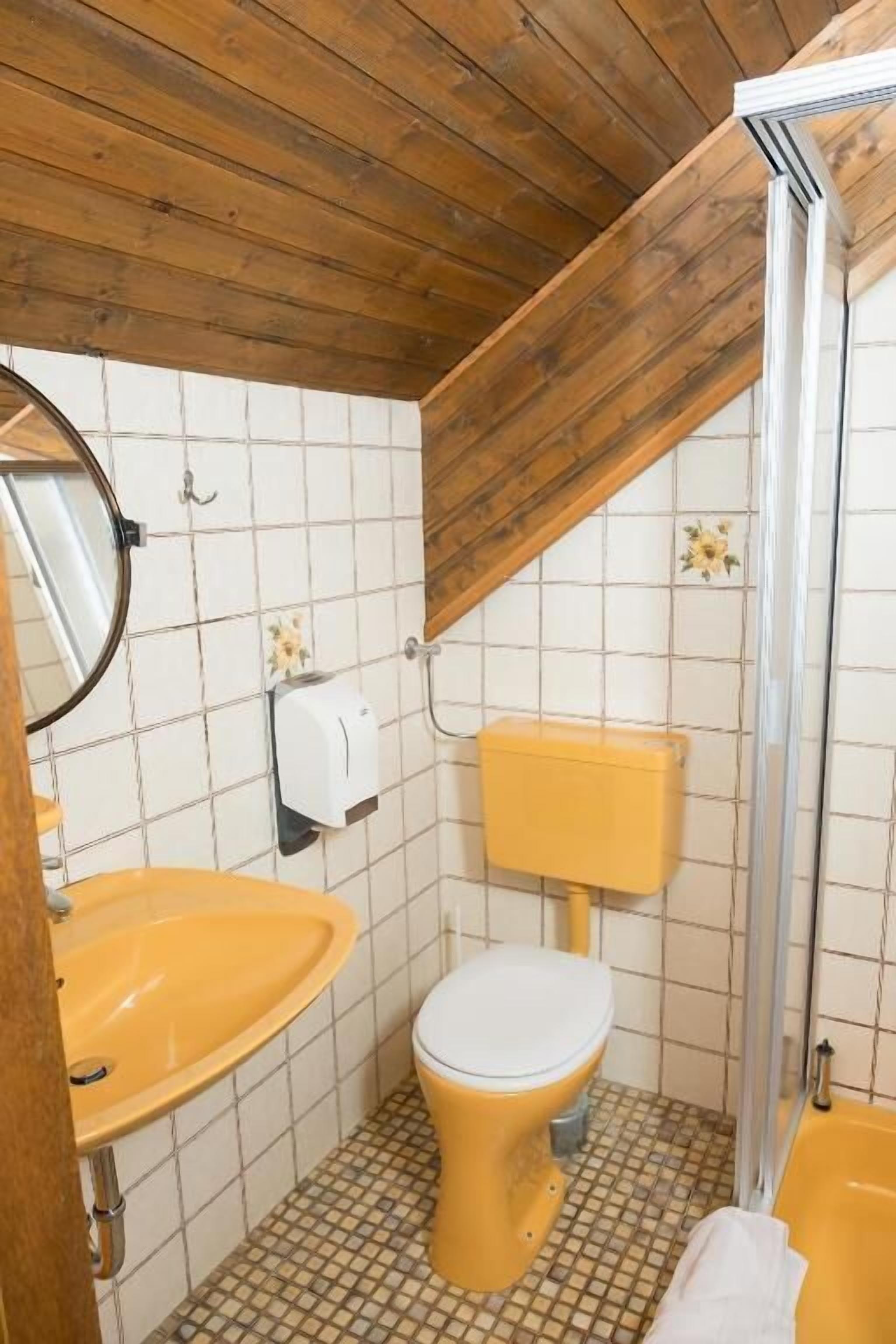 A bathroom with a wooden ceiling, a yellow sink, a white toilet, and a shower area.