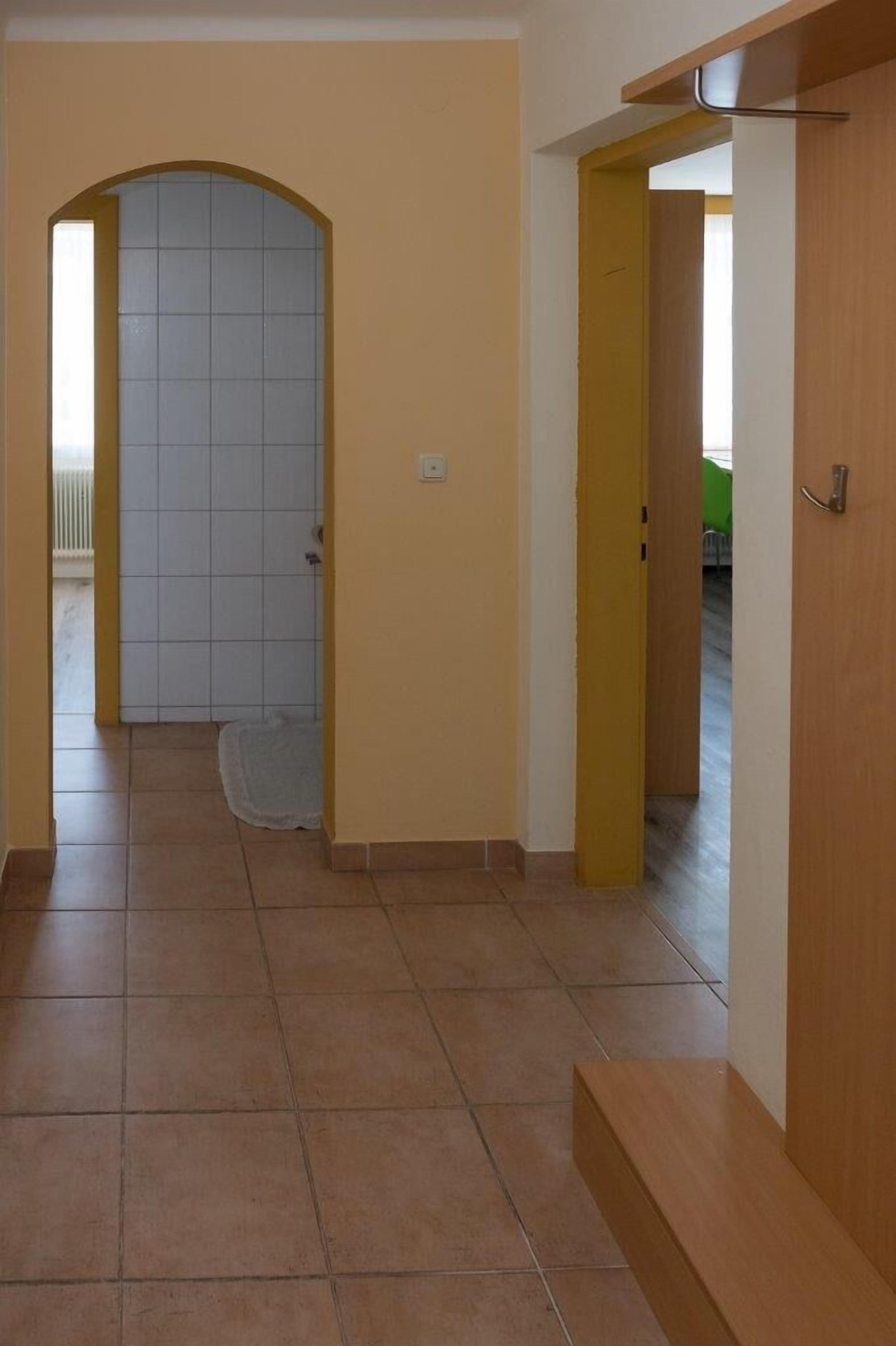 A hallway with a tiled floor, a door with a yellow frame, and a white door in the background.