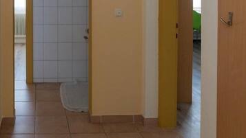 A hallway with a tiled floor, a door with a yellow frame, and a white door in the background.