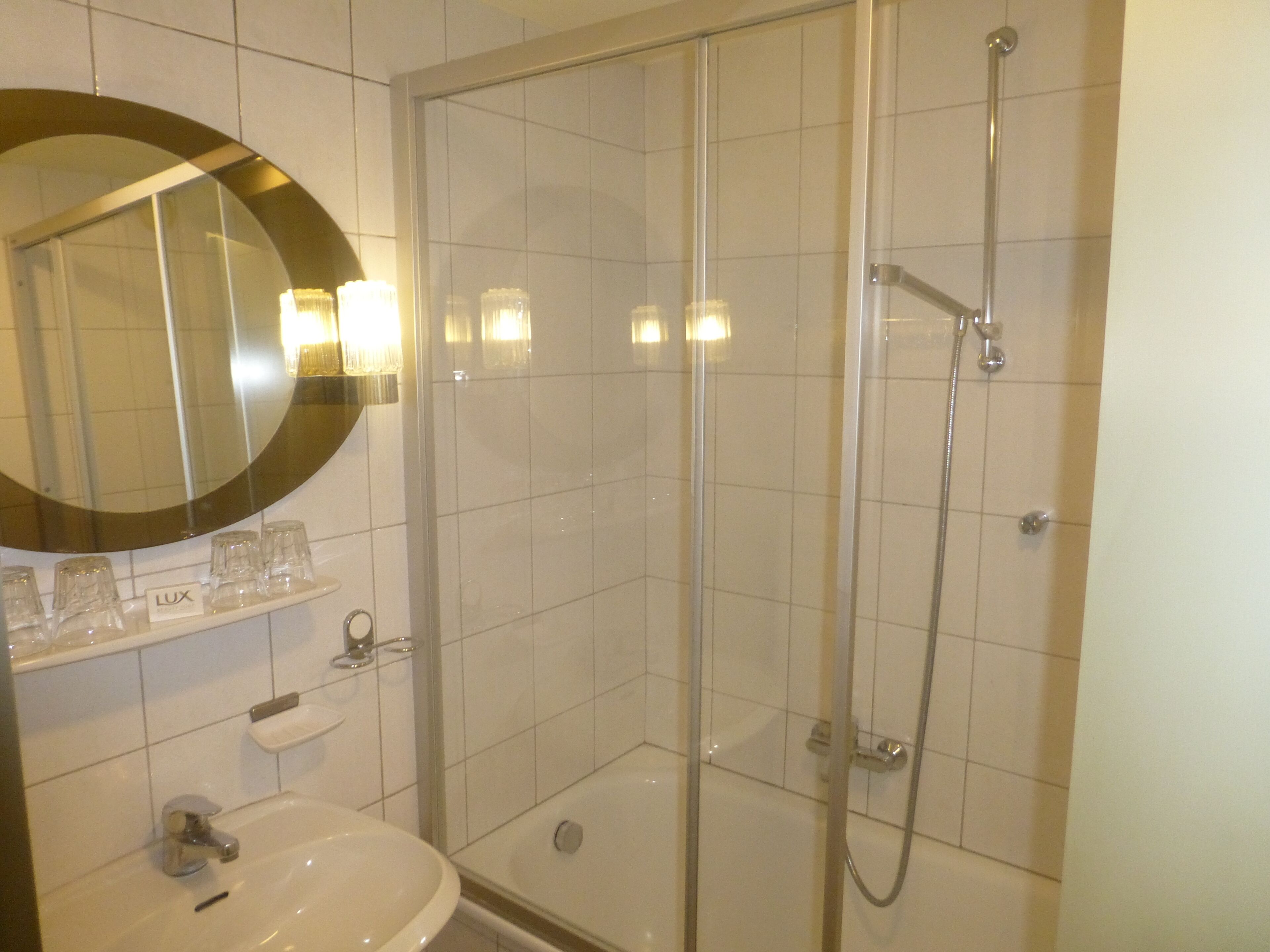 A bathroom with a glass-enclosed shower, a sink, and a mirror with a round frame.