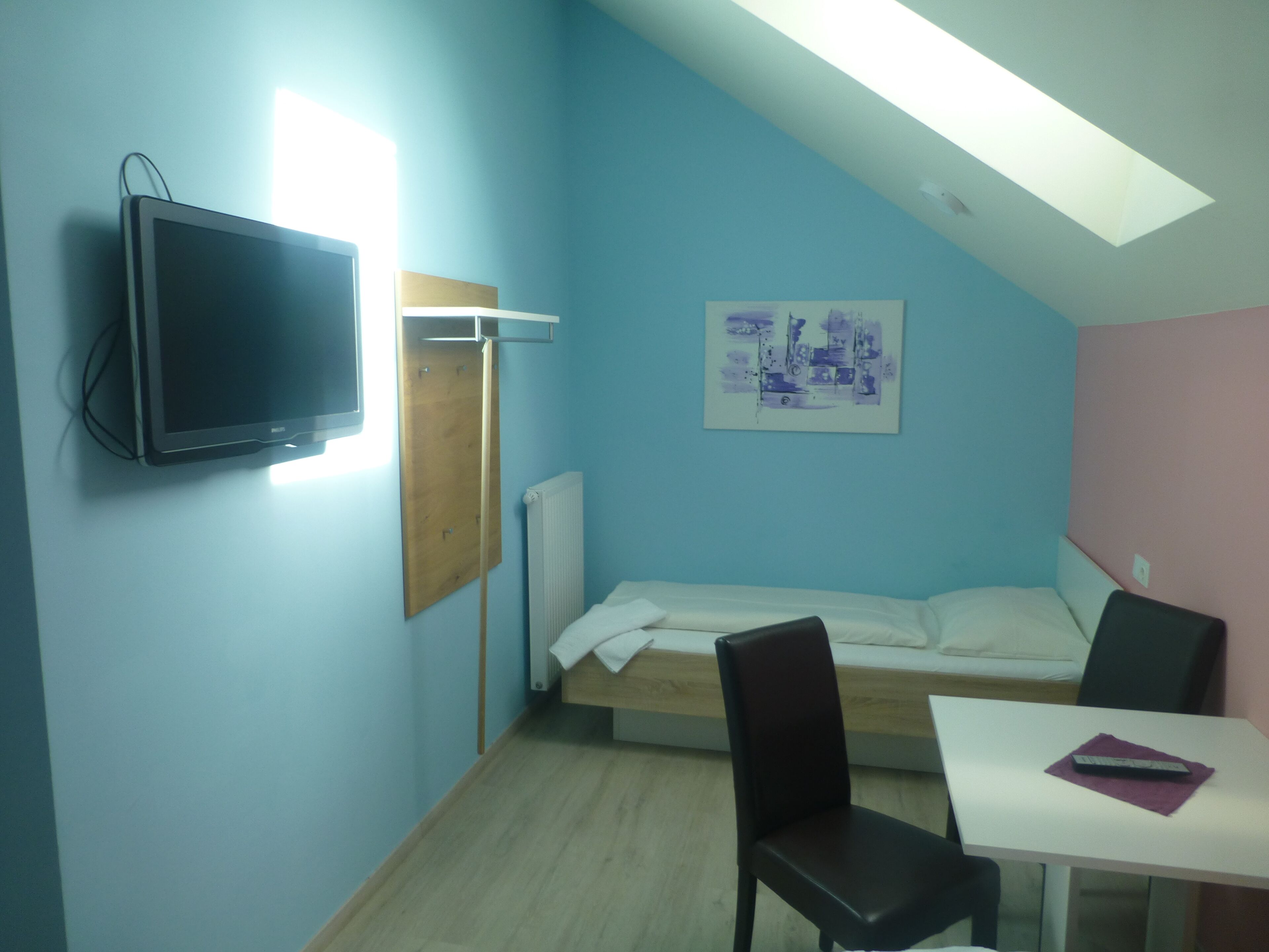 Een kamer met een bed, een bureau, een stoel, een televisie en een schilderij aan de muur.