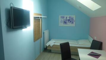Een kamer met een bed, een bureau, een stoel, een televisie en een schilderij aan de muur.