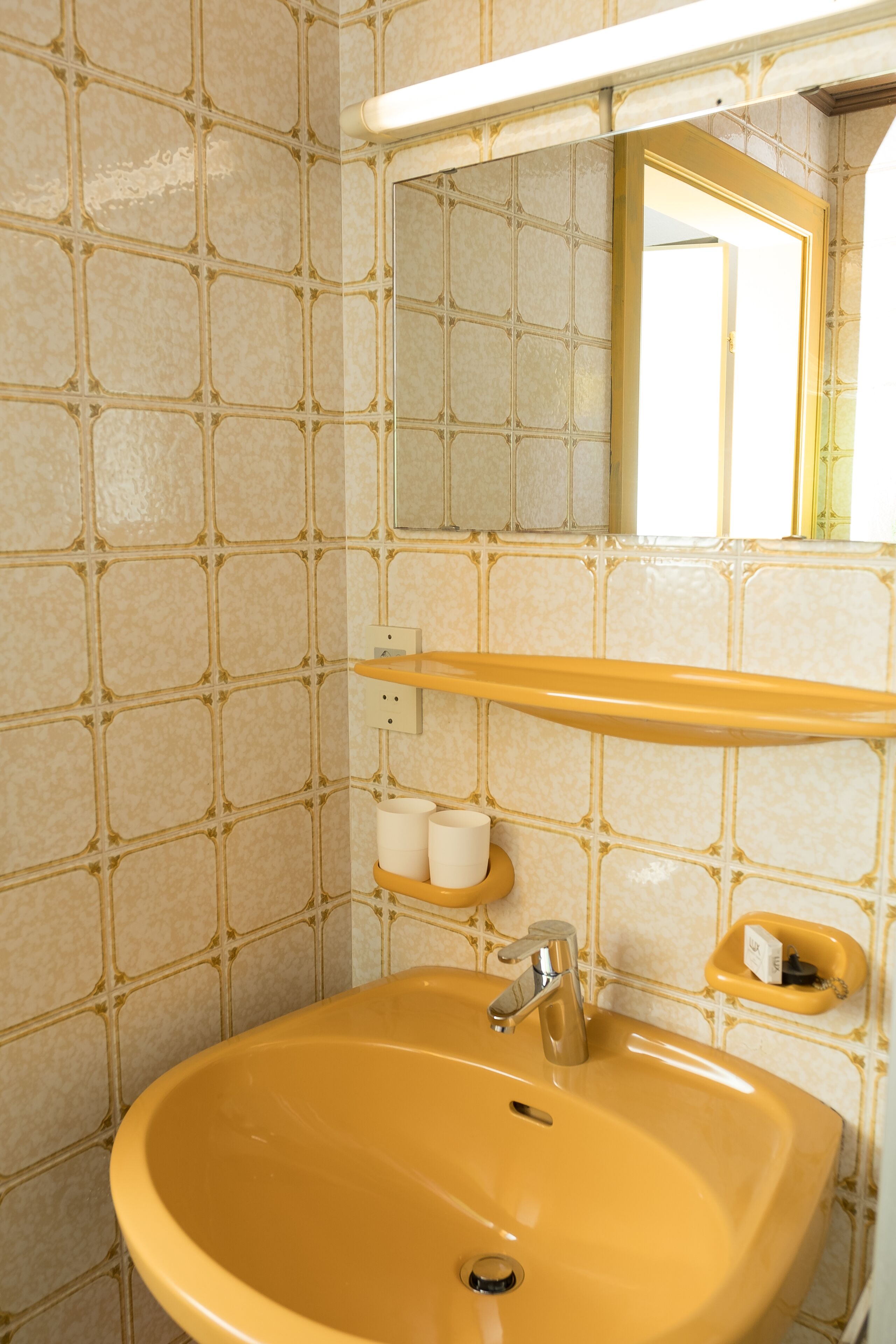 Un baño con un lavamanos color beige, un espejo encima y una pared con azulejos.