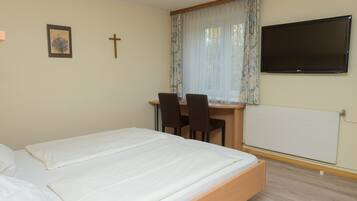 A bedroom with a bed, a desk with two chairs, a TV, and a window with curtains.