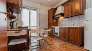 A compact kitchen with wooden cabinets, a white refrigerator, a stove, and a window with curtains. - WATER -  WHOLE APARTMENT 4 GUESTS (Biandrate)