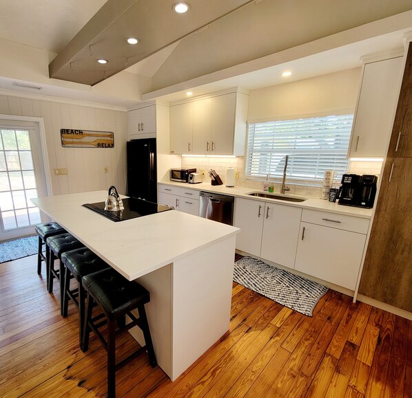 A modern kitchen with a central island, bar stools, a refrigerator, a microwave, and a coffee maker.