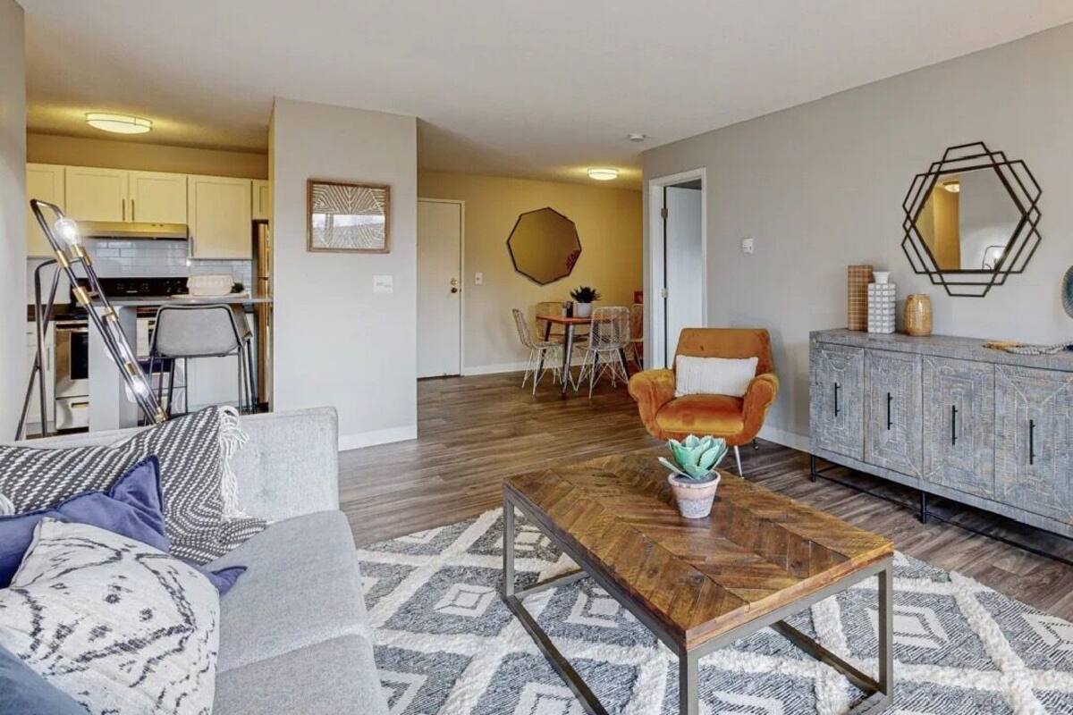 A modern living room with a sofa, coffee table, and a dining area in the background.