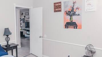 A bedroom with a bed, a nightstand, a lamp, a wall-mounted fan, and a door leading to another room.