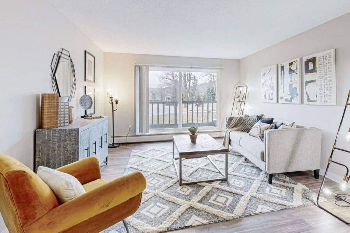 A modern living room with a sofa, armchair, coffee table, and artwork on the walls.