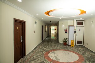 Pasillo de hotel con piso de mármol, alfombra circular estampada y una puerta de madera con el número 202.