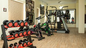 Ein Fitnessstudio mit Trainingsgeräten, darunter Kurzhanteln, ein Ergometer und ein Laufband.