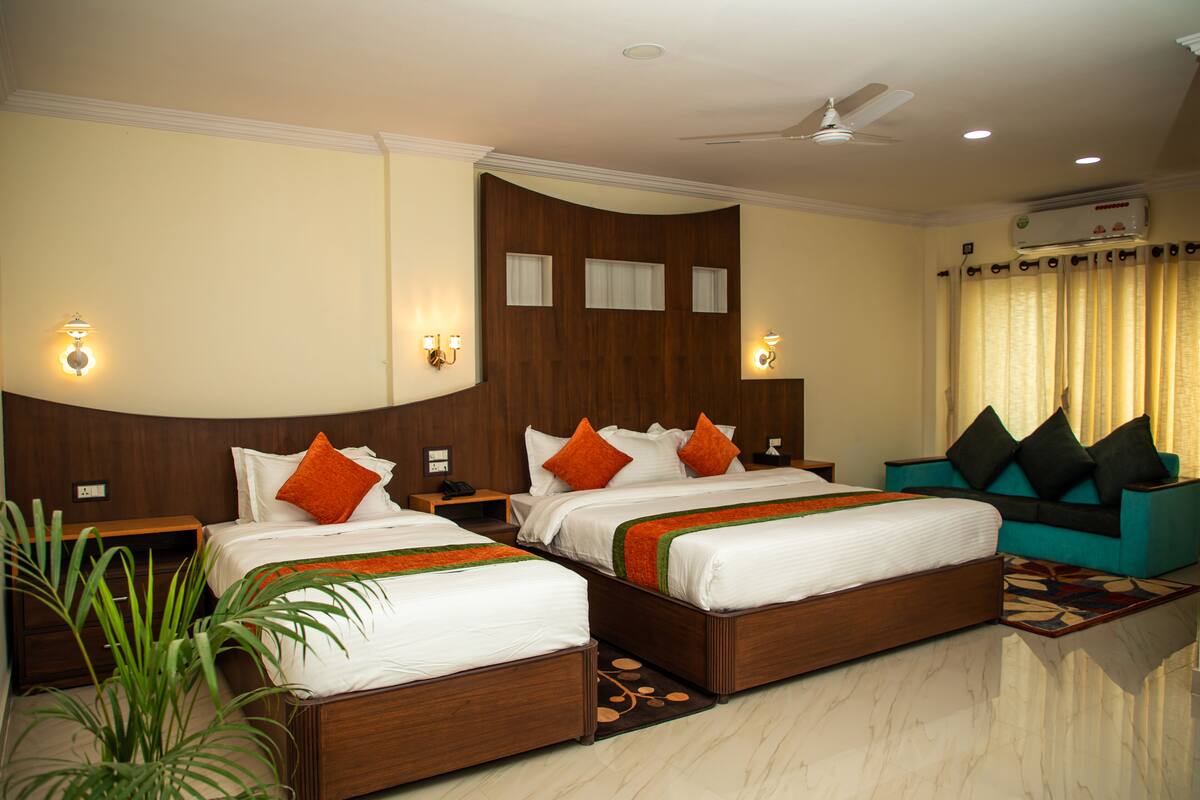 A hotel room with two beds, a sofa, a ceiling fan, and an air conditioning unit.