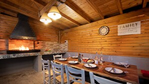 A rustic wooden interior with a fireplace, wooden ceiling beams, and a dining table set for four with white chairs. - Villa Serenity (Corfu)