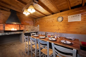 A rustic wooden interior with a fireplace, wooden ceiling beams, and a dining table set for four with white chairs.