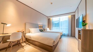A hotel room with a large bed, a desk with a chair, a TV, and a plant.