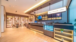 A modern coffee shop interior with a reception desk, shelves with books, and a digital menu display.