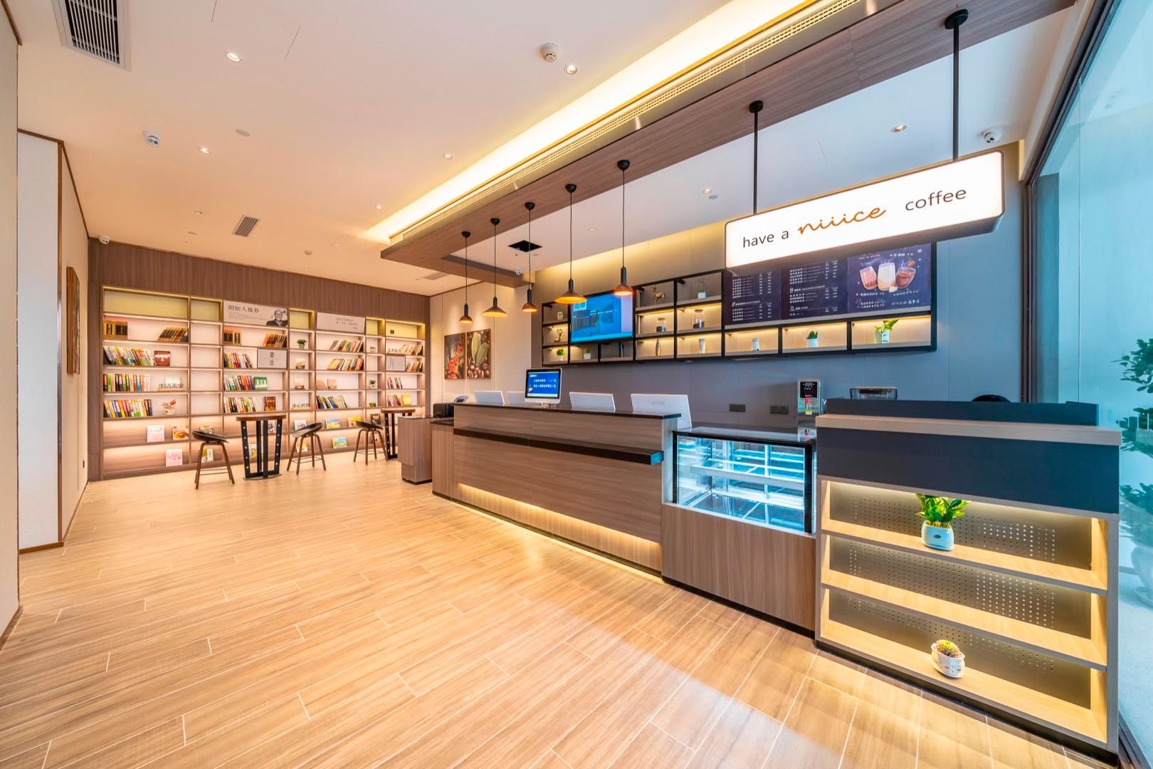 A modern coffee shop interior with a reception desk, shelves with books, and a digital menu display.