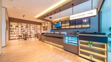 A modern coffee shop interior with a reception desk, shelves with books, and a digital menu display.