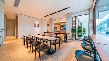 A modern dining area with a long table, multiple chairs, and a kitchen visible in the background.