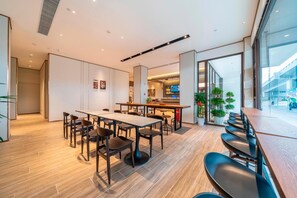 A modern dining area with a long table, multiple chairs, and a kitchen visible in the background. - Hanting Hotel (Chongqing)