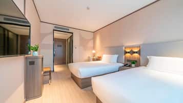 A hotel room with two beds, a desk, a mirror, and a door leading to another room.
